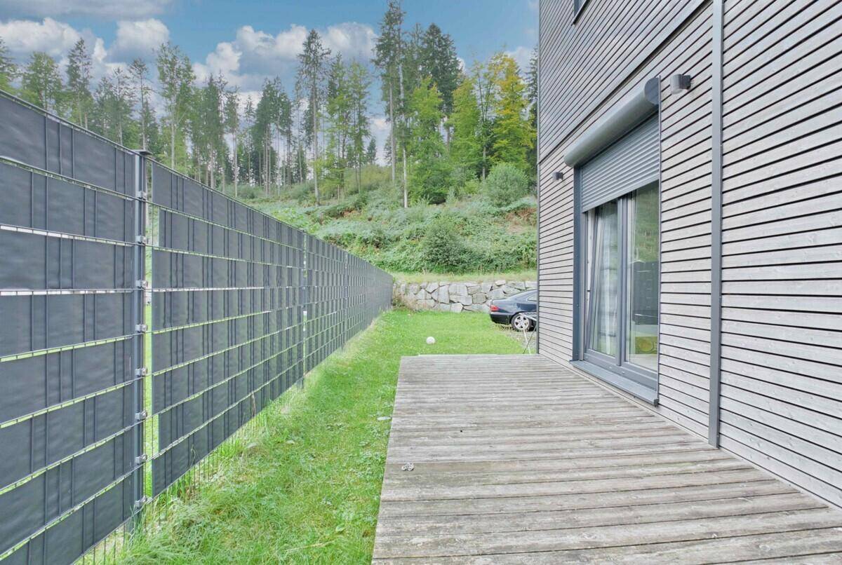 Gartenbereich mit Holzterrasse, Rasenfläche und blickgeschütztem Zaun zum Waldrand.