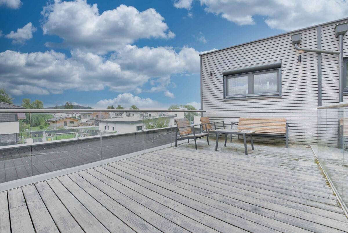 Geräumige Dachterrasse mit Holzbelag, Glasgeländer und Sitzgelegenheiten im Freien.