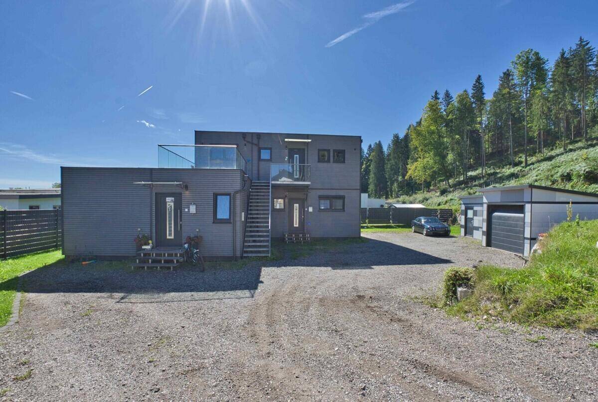 Gesamtansicht des modernen Anwesens mit Hauptgebäude, Garage und weitläufiger Kiesauffahrt vor Waldkulisse.
