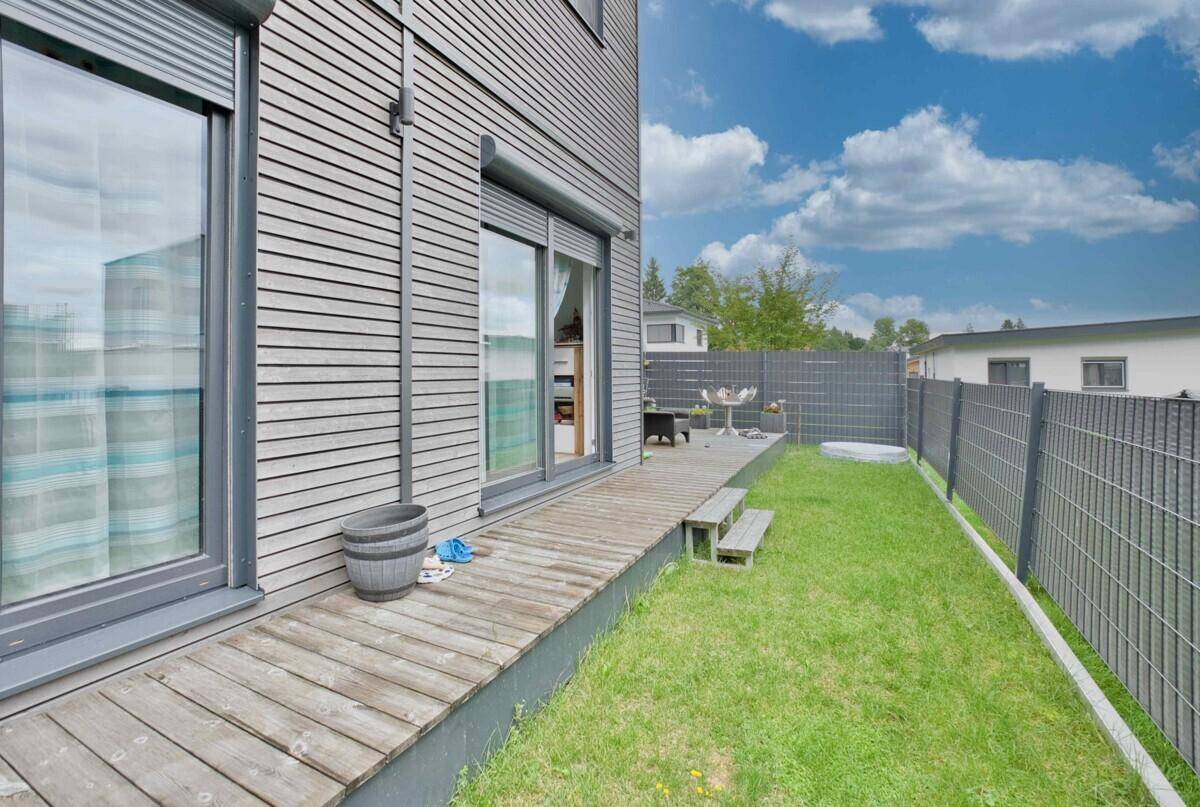 Seitlicher Außenbereich mit Holzterrasse, Rasenfläche und großen Schiebetüren zum Haus.