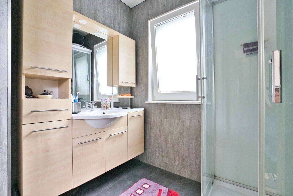 Badezimmer mit Duschkabine, Waschtisch und hohem Spiegelschrank für Stauraum.