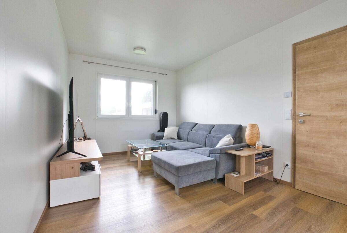 Gemütliches Wohnzimmer mit grauem Sofa, Holzboden und einer modernen Holztür.