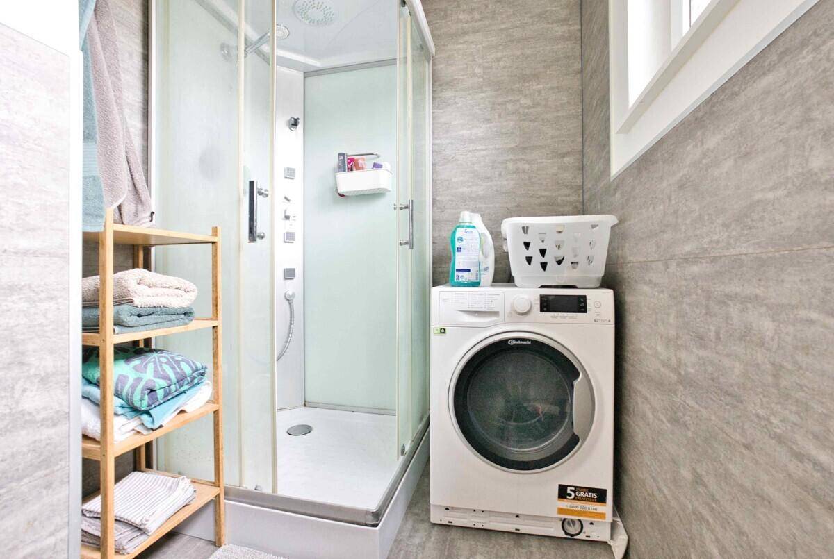 Modernes Badezimmer mit Duschkabine, Waschmaschine und grauen Wandfliesen.