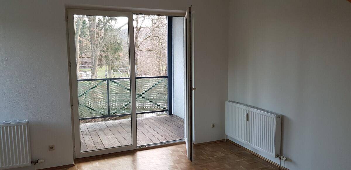 Heller Raum mit Zugang zu einem Balkon mit Holzfußboden und Blick ins Grüne.