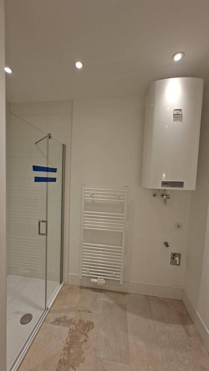 Badezimmer mit Duschkabine, beheiztem Handtuchhalter und Warmwasserboiler an der Wand.