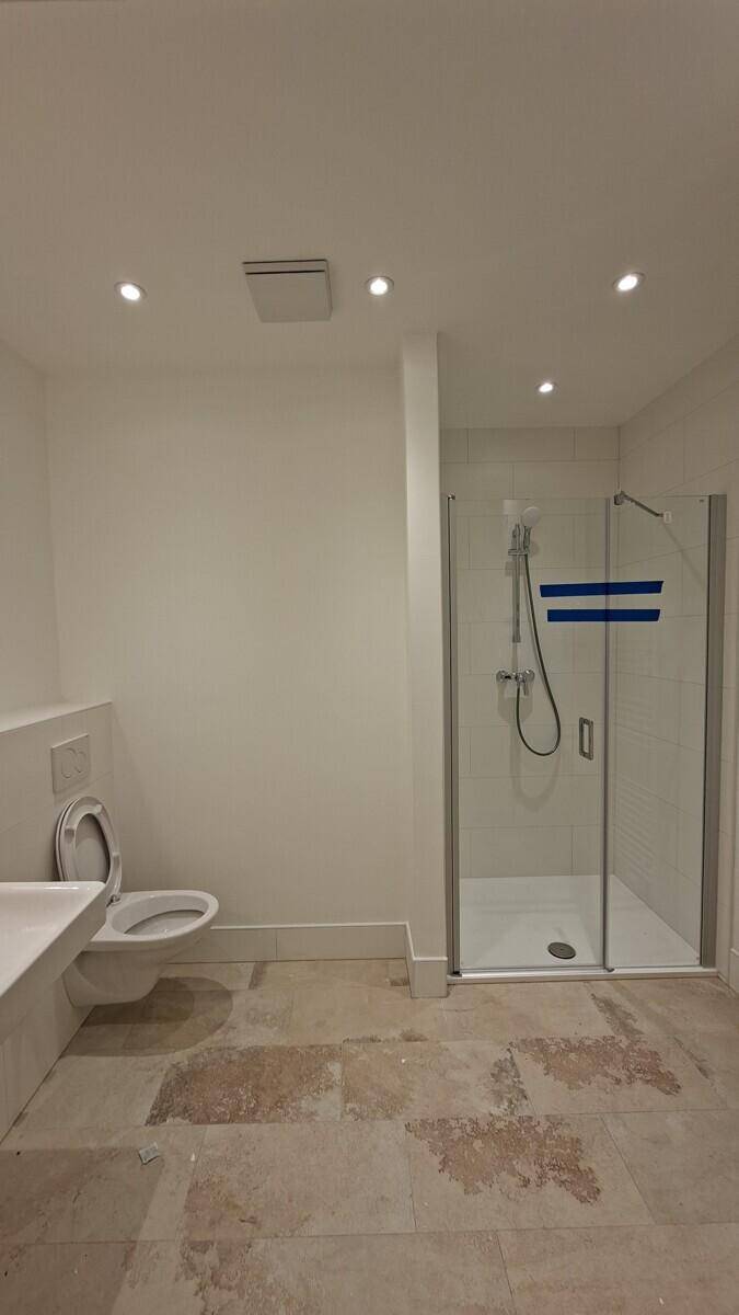 Modernes Badezimmer mit Duschkabine und wandhängendem WC, der Boden ist noch nicht fertiggestellt.