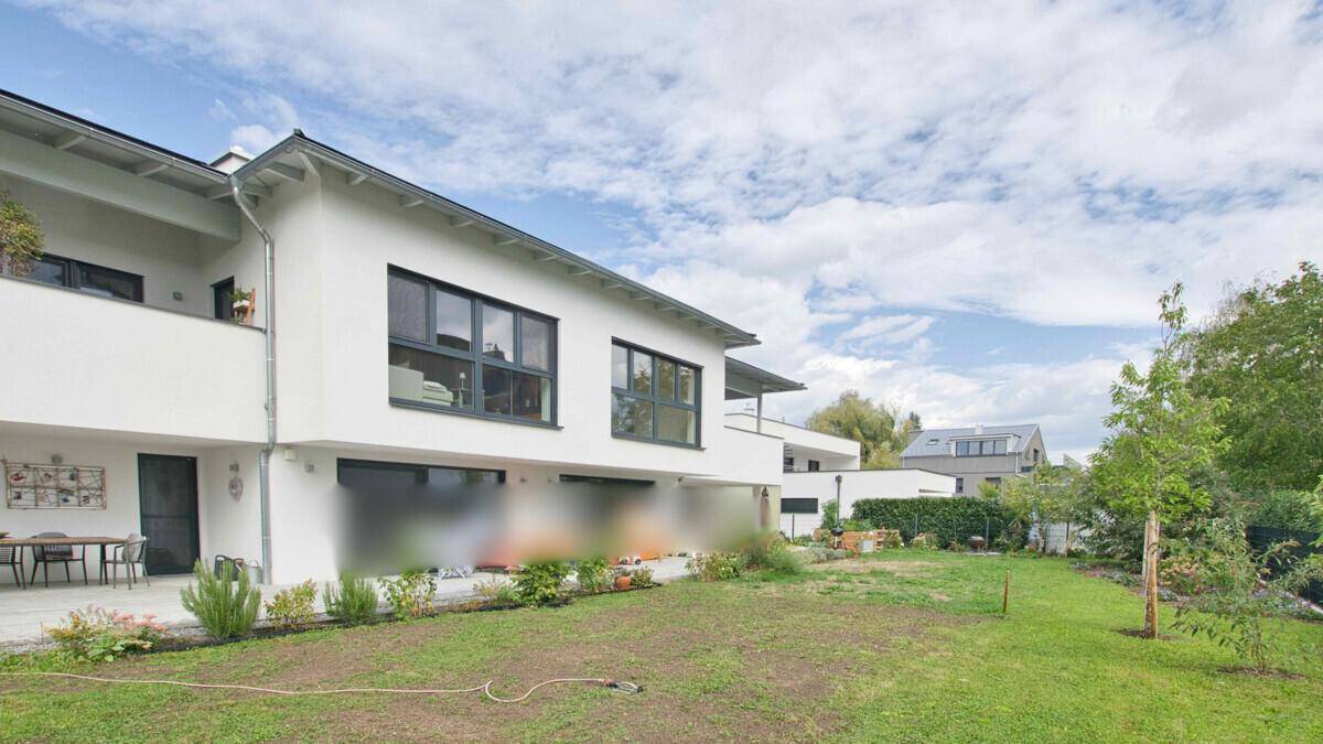Moderne weiße Hausfassade mit großem Rasenbereich und einer Terrasse mit Sitzgelegenheiten.