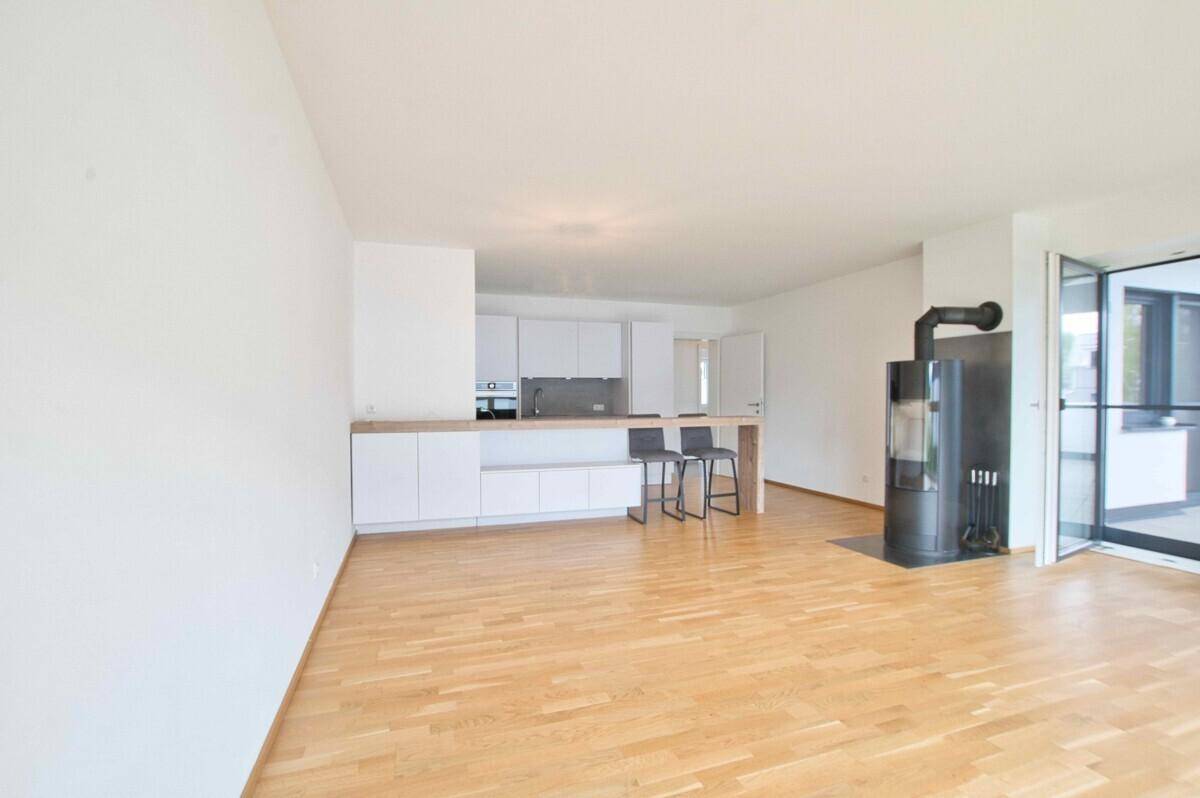 Geräumiger offener Wohnbereich mit Holzboden, Kaminofen und Zugang zu einem Außenbereich.