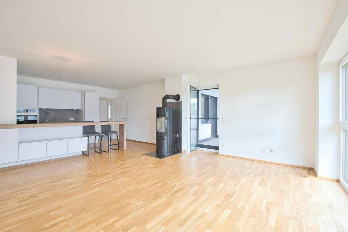 Heller offener Wohnbereich mit Holzboden, Kaminofen und großen Fenstern.