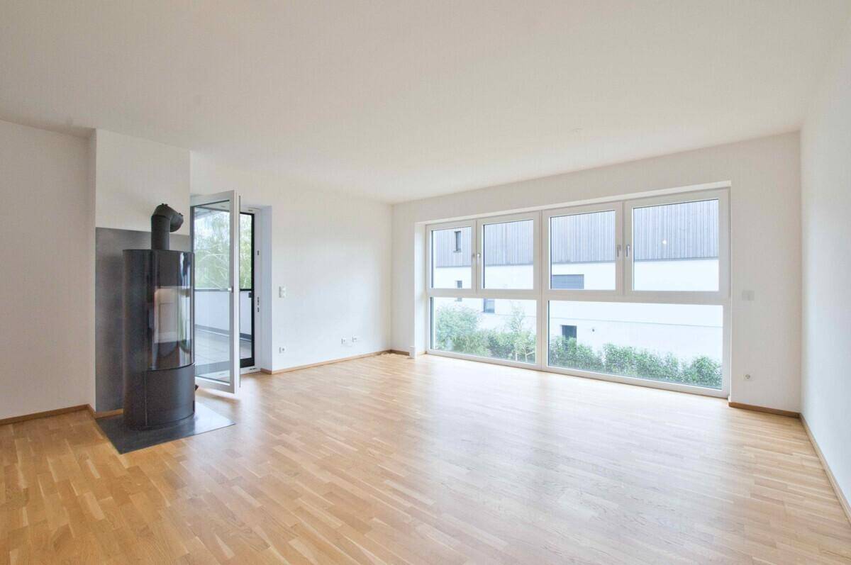 Geräumiges Wohnzimmer mit Kaminofen, großen Fenstern und Blick ins Grüne.