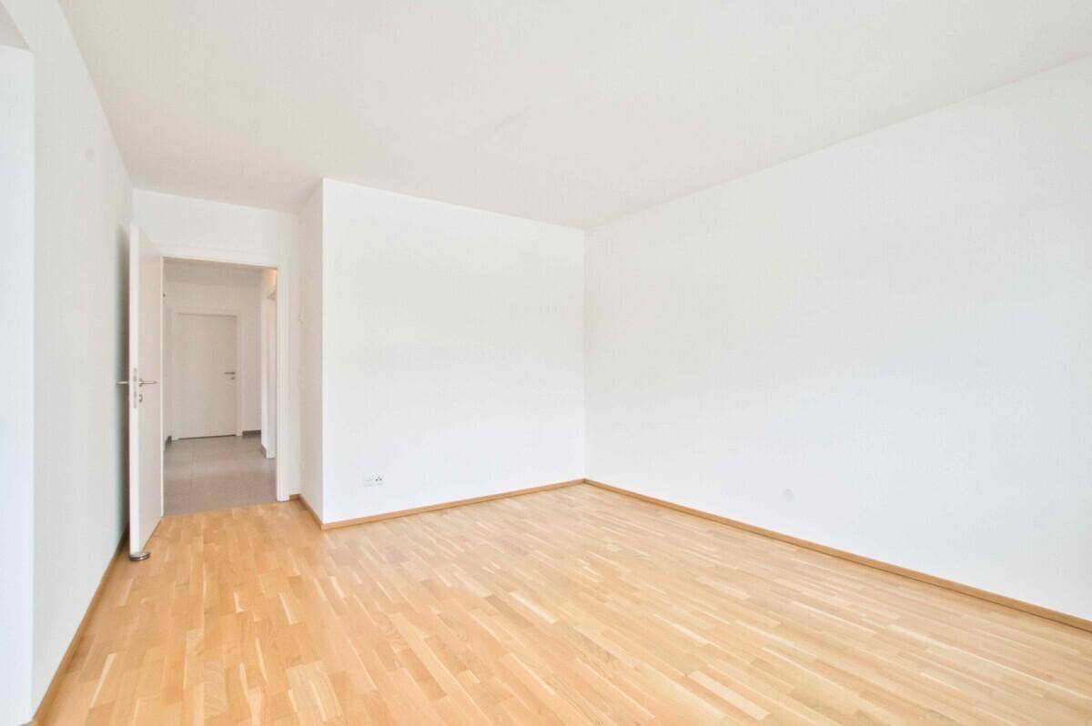 Leerer Raum mit hellem Parkettboden und weiß gestrichenen Wänden.
