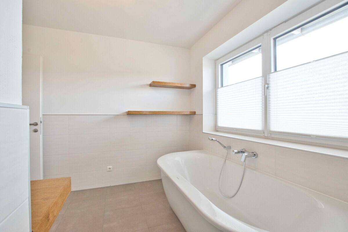 Helles Badezimmer mit freistehender Badewanne und großem Fenster.