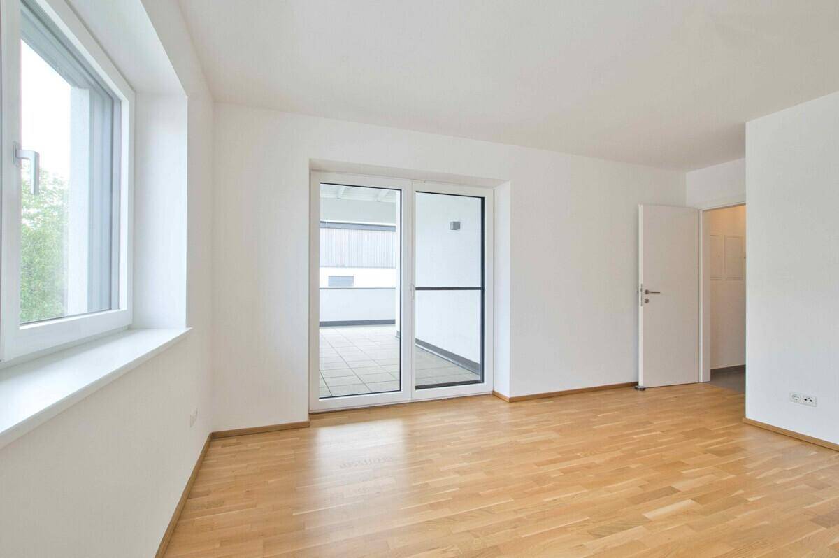 Geräumiges Zimmer mit Parkettboden, großen Fenstern und Zugang zum Balkon.