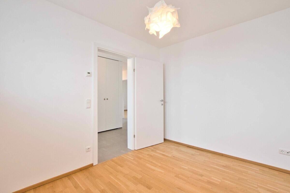 Leerer Raum mit hellem Parkettboden und weiß gestrichenen Wänden.