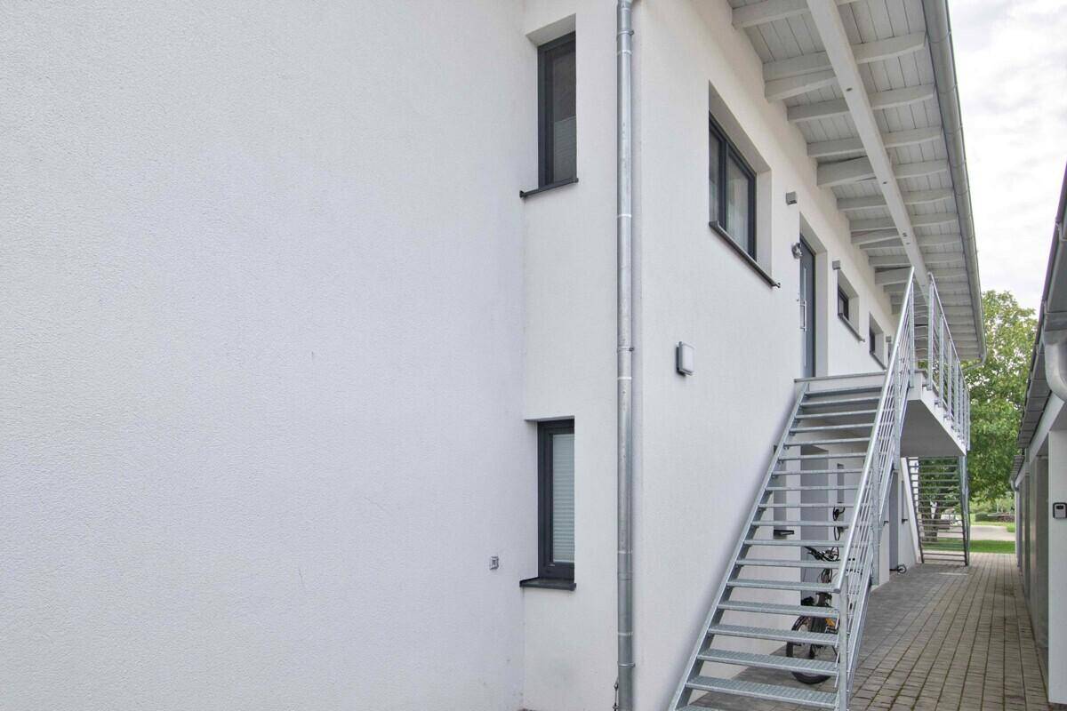 Weiße Hausfassade mit externer Metalltreppe, die zu den oberen Etagen führt.