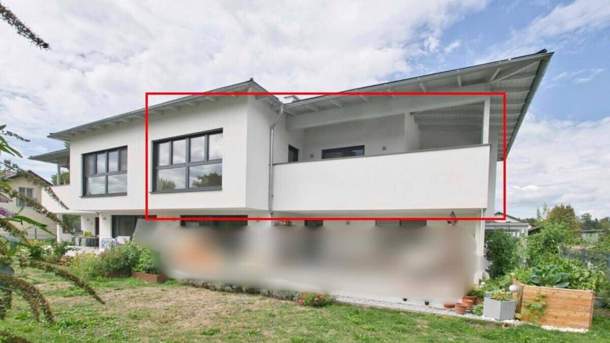 Moderne weiße Hausfassade mit Balkon, umrahmt von einem roten Rechteck, vor grünem Garten.