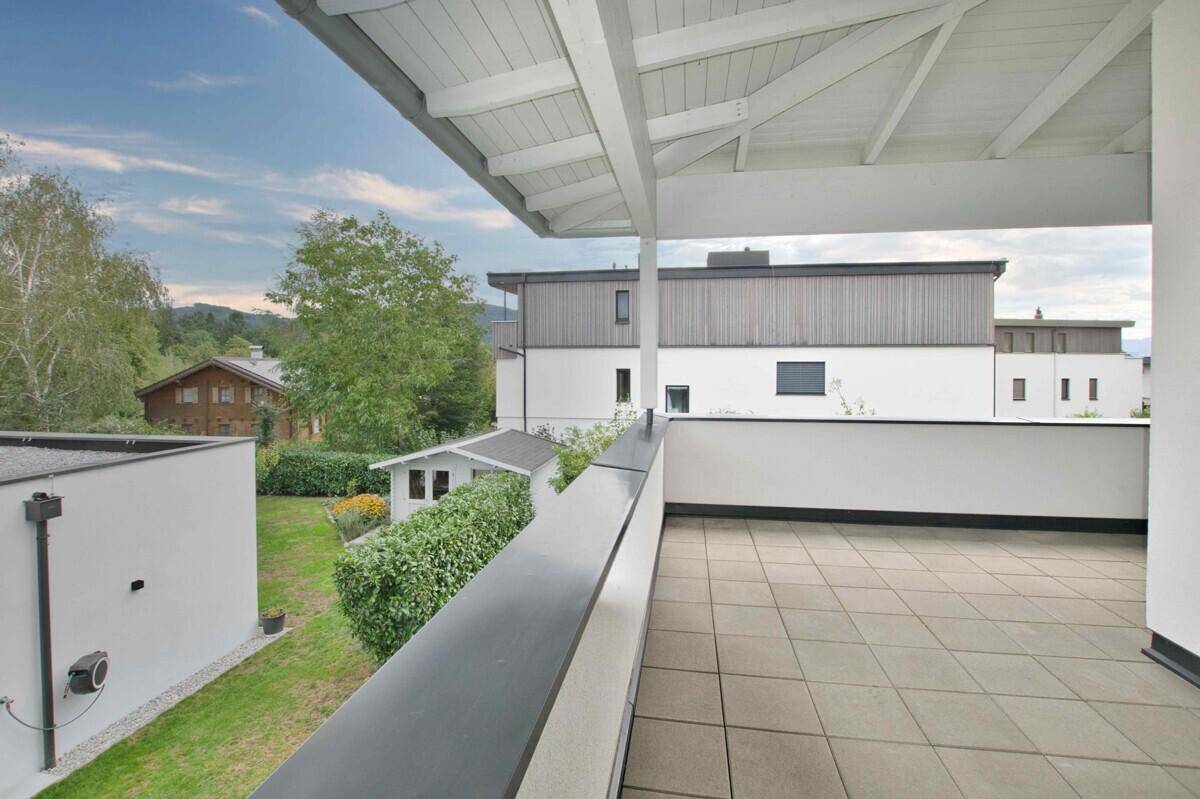 Geräumiger Balkon mit Fliesenboden, Überdachung und Blick auf den Garten und die Umgebung.