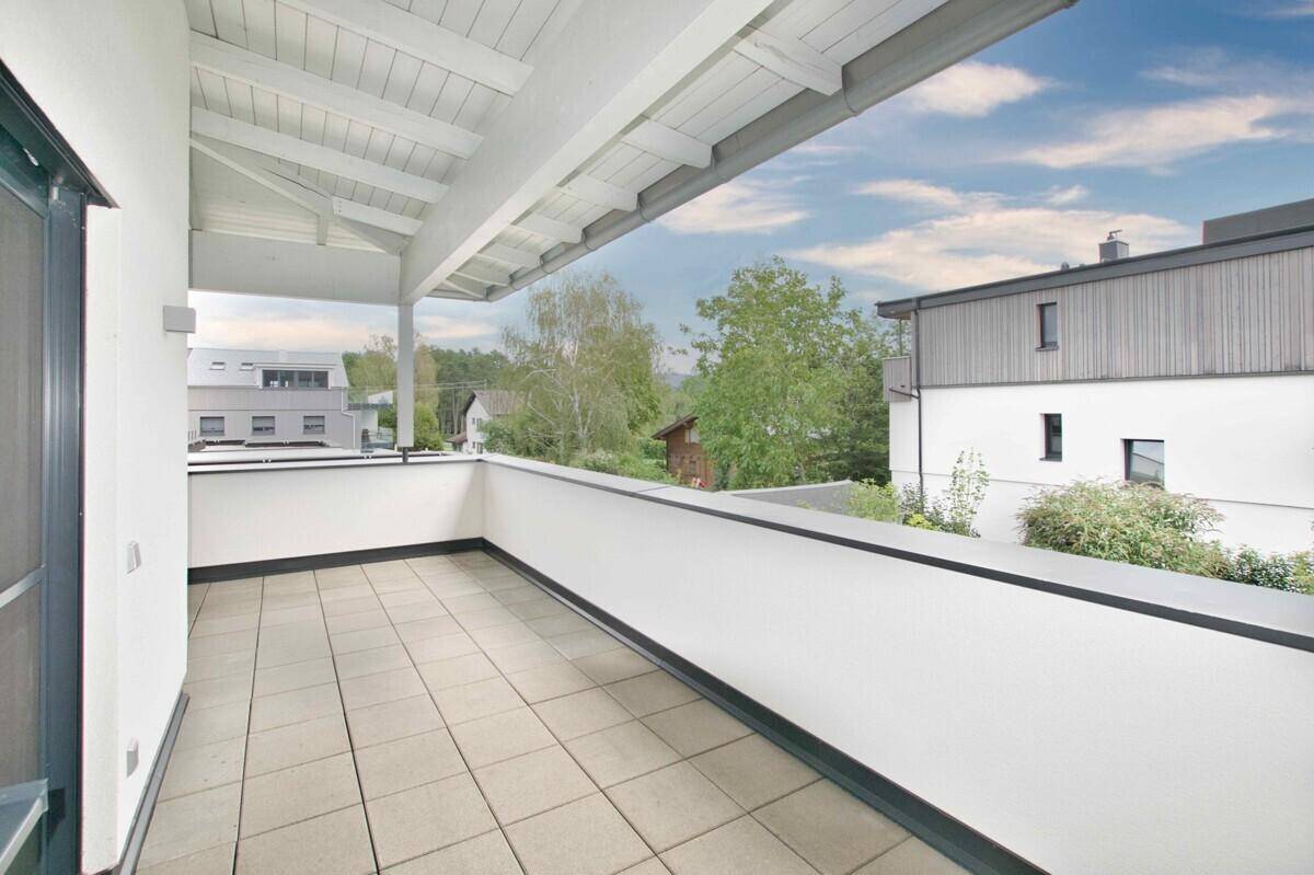 Großer überdachter Balkon mit Fliesenboden und Blick auf die Umgebung.