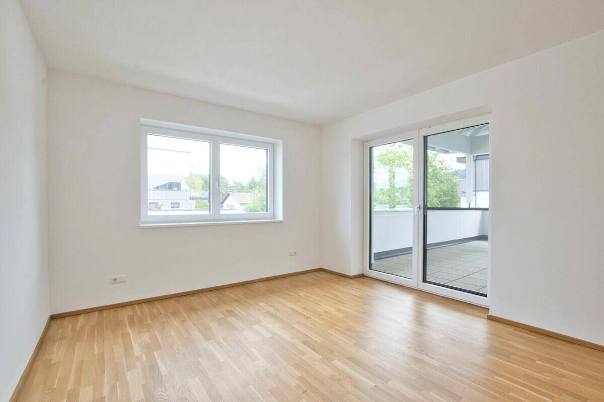 Helles Zimmer mit Parkettboden, Fenster und Schiebetür zum Balkon.