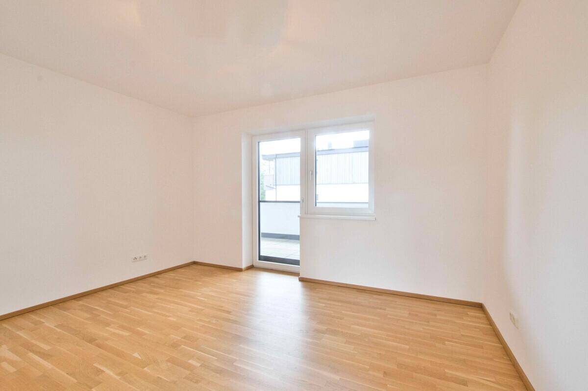 Helles Zimmer mit Parkettboden und Zugang zu einem kleinen Balkon.