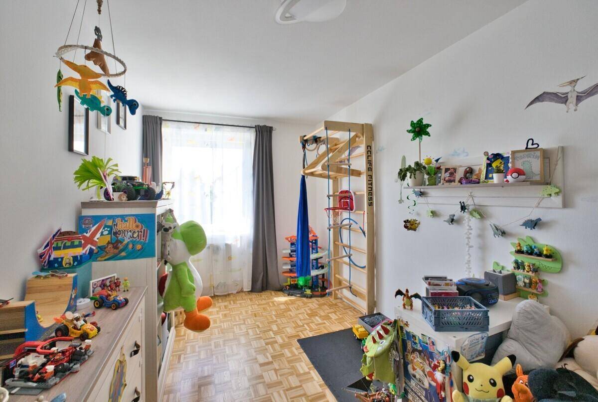 Helles Kinderzimmer mit Spielgeräten, bunten Dekorationen und Parkettboden.