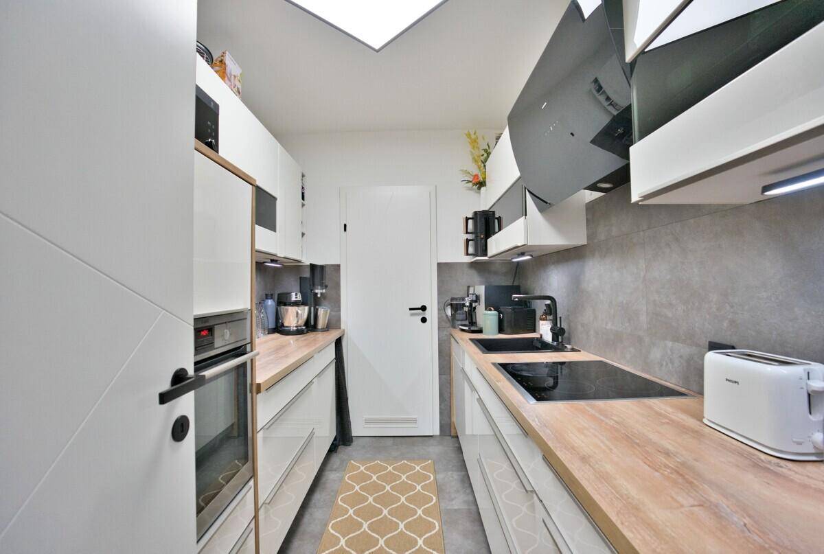 Moderne Küche mit weißen Hochglanzfronten, Holz-Arbeitsplatten und integrierten Geräten.
