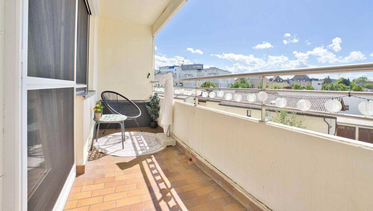 Sonniger Balkon mit Fliesenboden, Sitzgelegenheit und Blick auf die Umgebung.