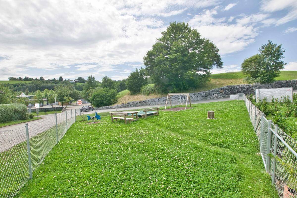 Weitläufiger Spielbereich mit Rasenfläche, Schaukel und Picknicktisch, umgeben von Natur.