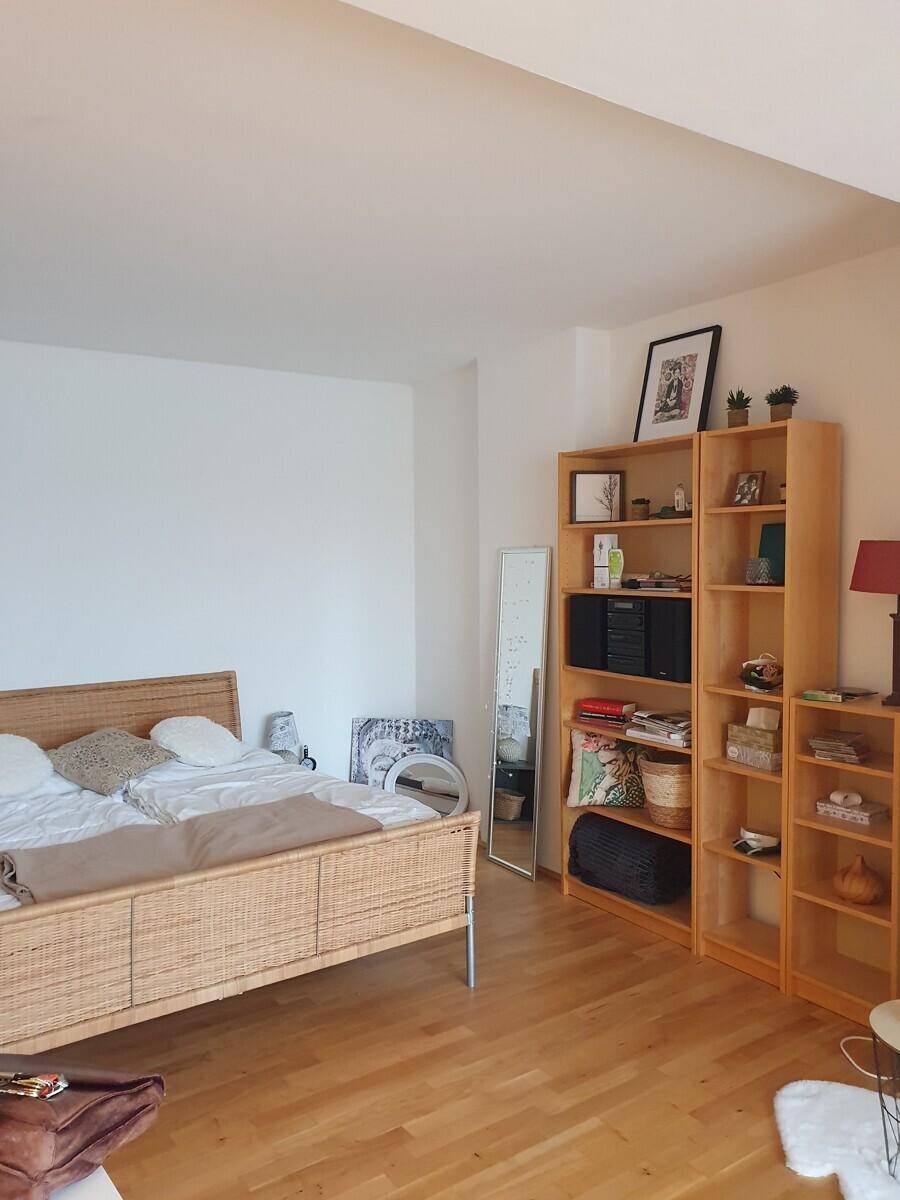Helles Schlafzimmer mit Rattanbett, Holzregalen und Parkettboden, bietet viel Stauraum.