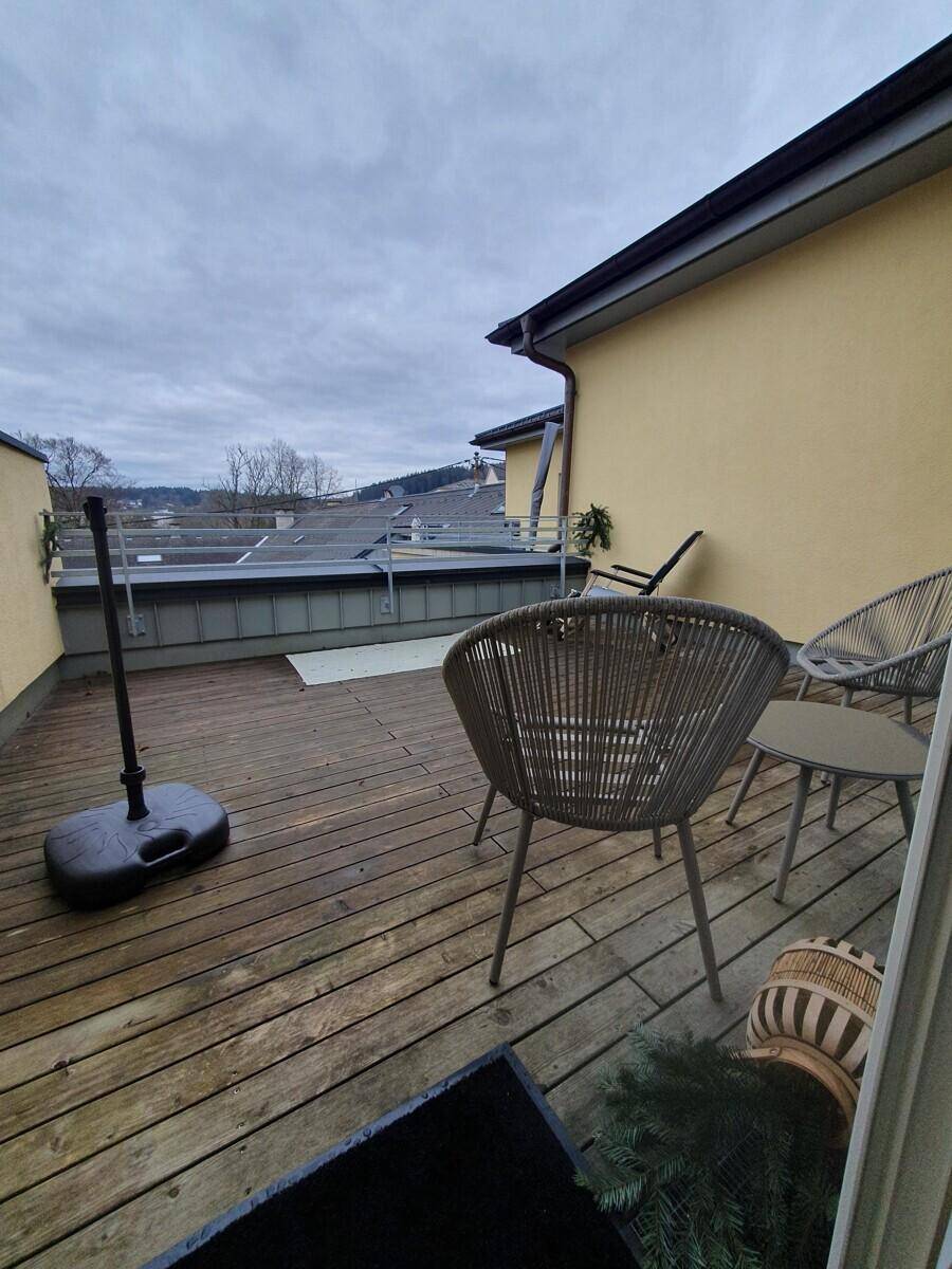 Geräumige Holzterrasse mit Sitzgelegenheiten und Blick auf die umliegenden Dächer und Bäume.