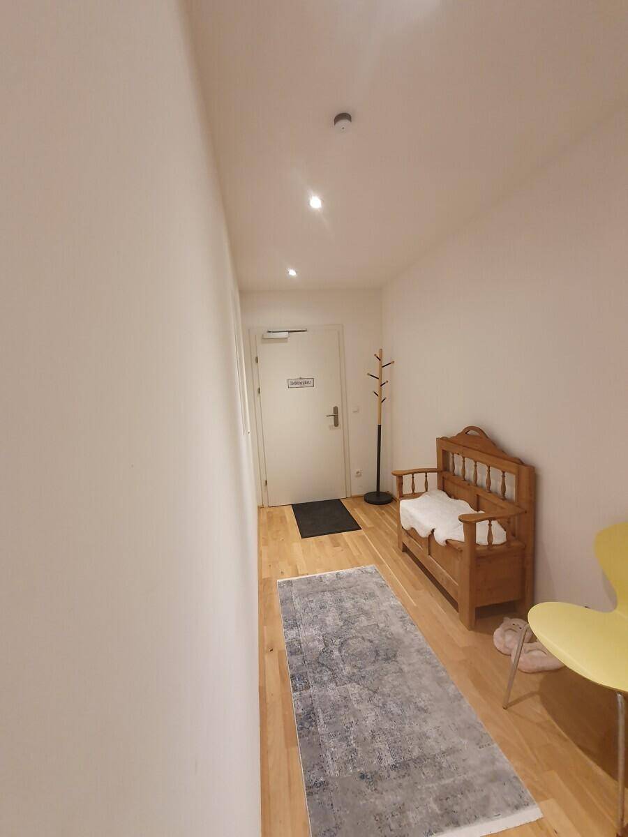 Langer, heller Flur mit Holzfußboden und einer traditionellen Holzbank am Eingangsbereich.