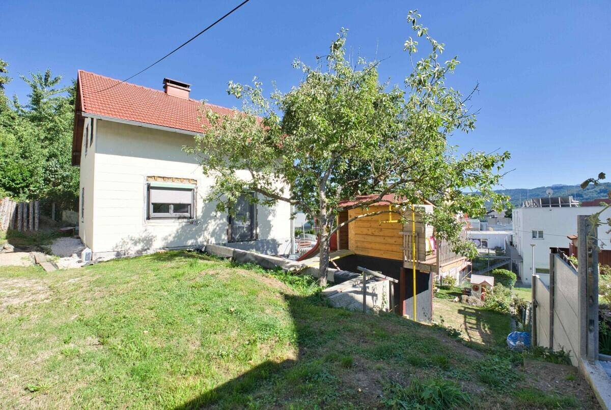 Seitenansicht des Hauses mit Garten, Obstbaum und Blick auf die Umgebung.
