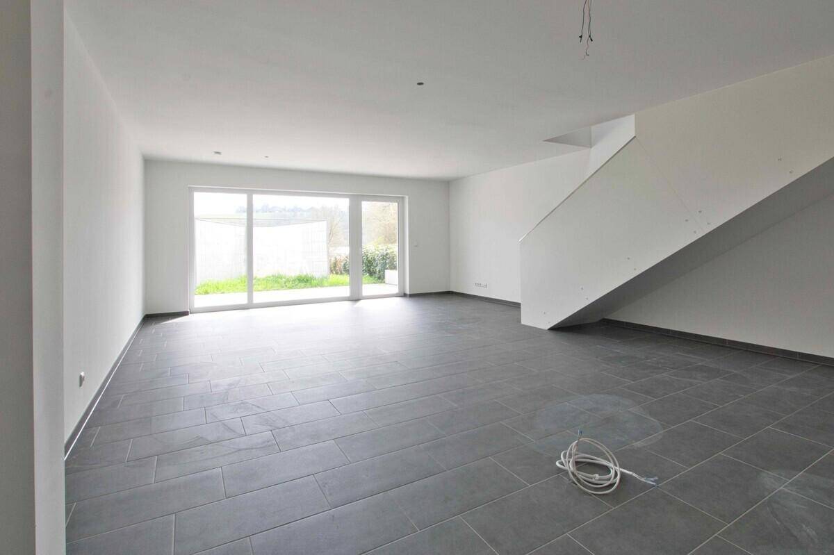 Heller Wohnbereich mit Fliesenboden, Zugang zur Terrasse und moderner Treppe.