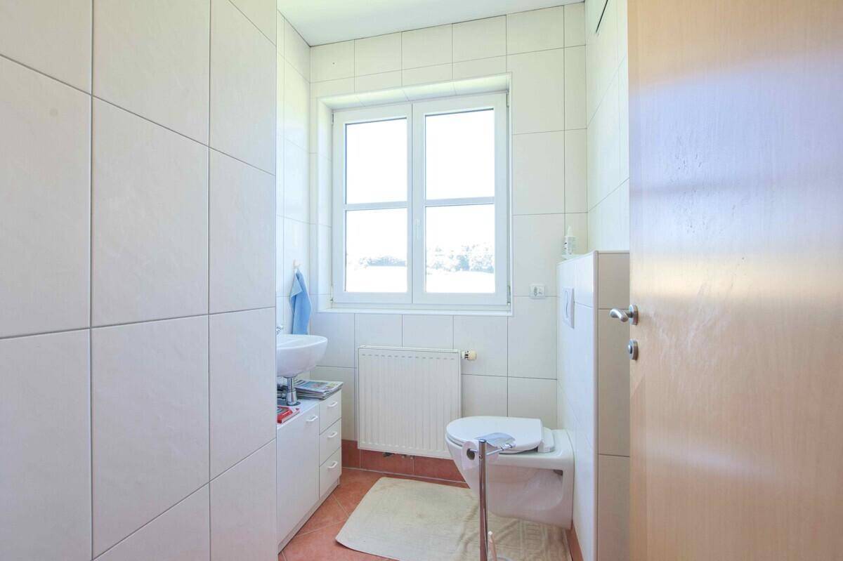 Helles Gäste-WC mit weißen Fliesen, Terrakottaboden und einem Fenster.