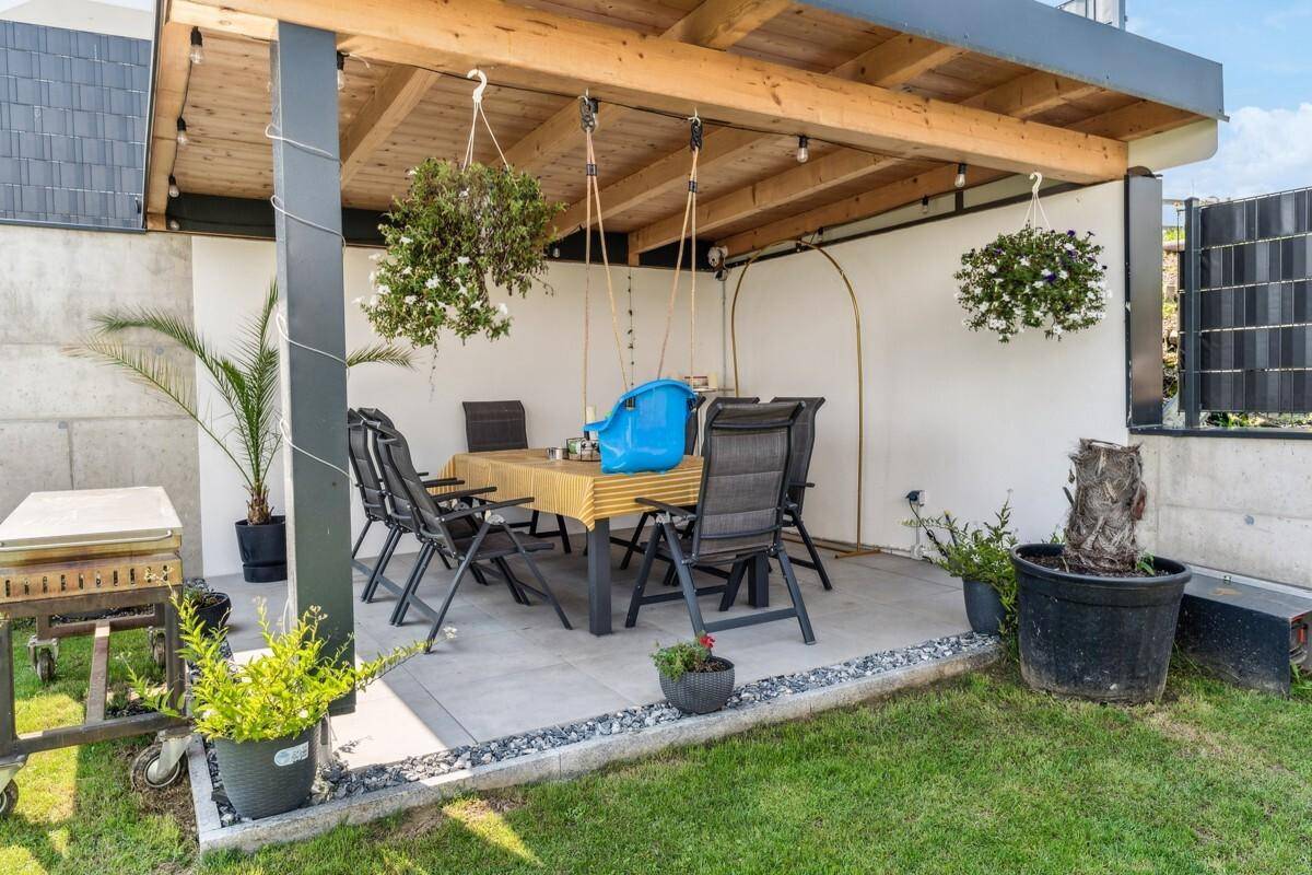 Überdachte Terrasse im Garten mit Esstisch und Stühlen für Mahlzeiten im Freien.
