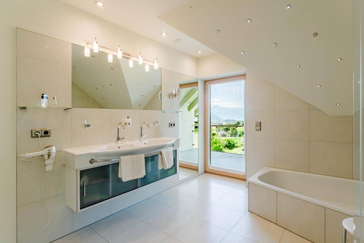 Helles Badezimmer mit elegantem Doppelwaschbecken, Badewanne und Fenster mit schöner Aussicht.