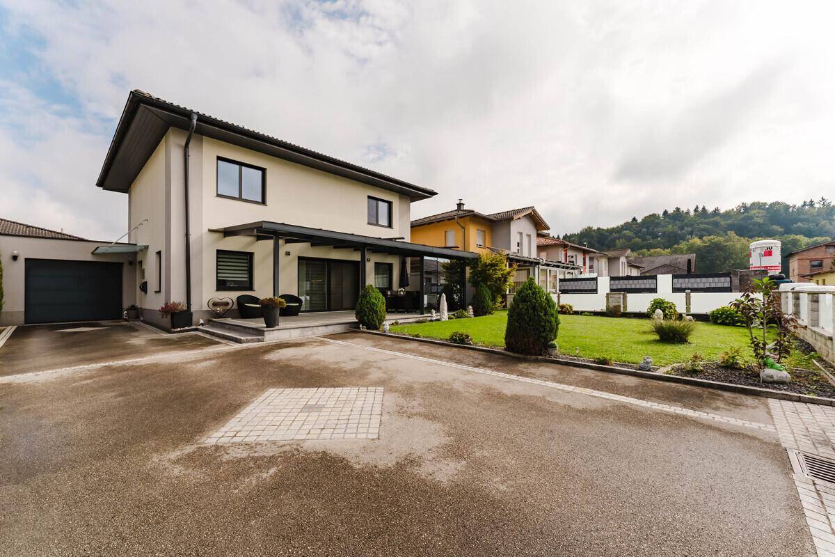 Modernes Einfamilienhaus mit großer Auffahrt, gepflegtem Rasen und überdachter Terrasse.