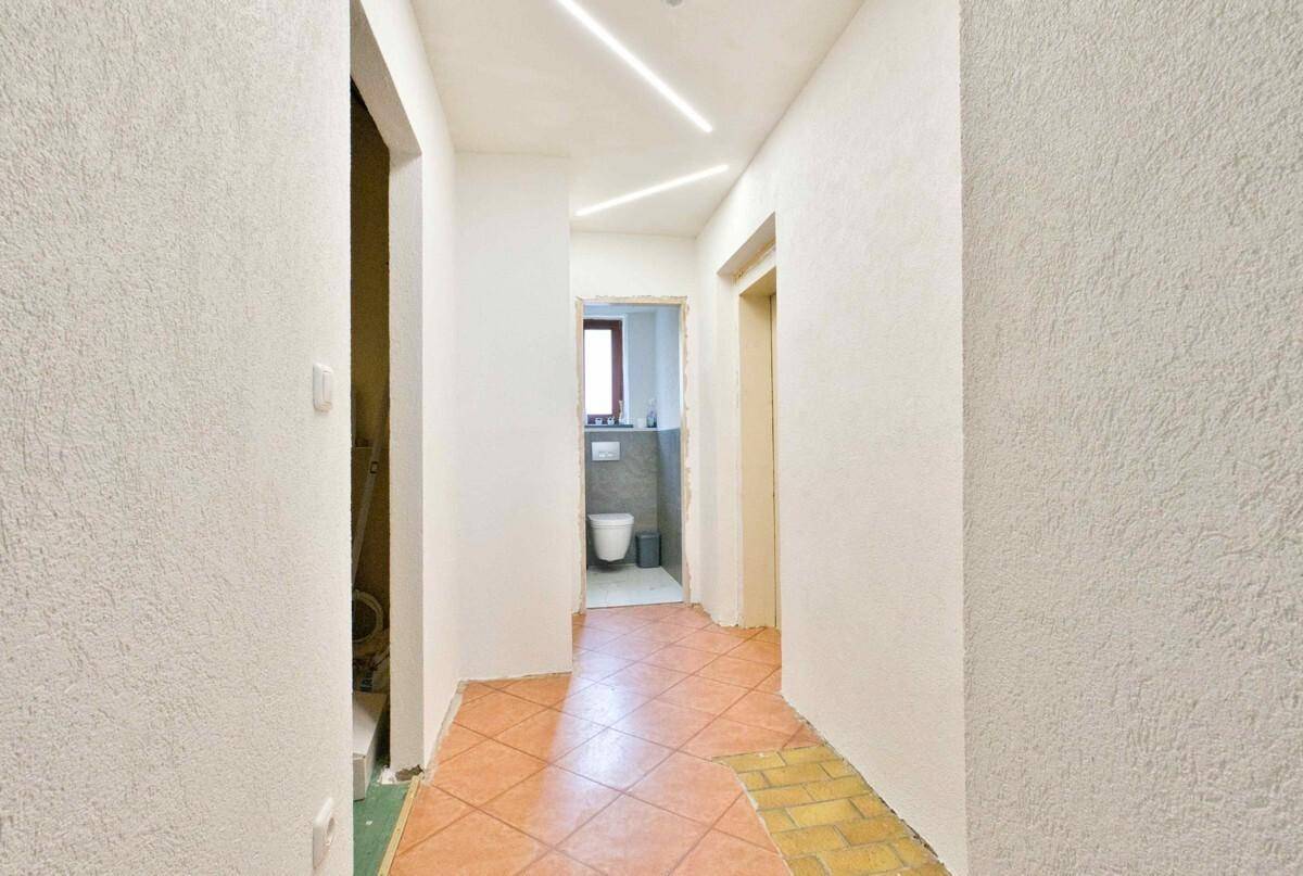 Flur mit Terrakotta-Fliesen und strukturierten Wänden, der zu einem Badezimmer führt.