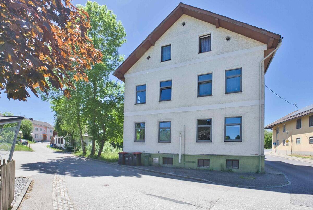 Mehrstöckiges Gebäude mit heller Fassade und Satteldach an einer Straßenecke unter blauem Himmel.