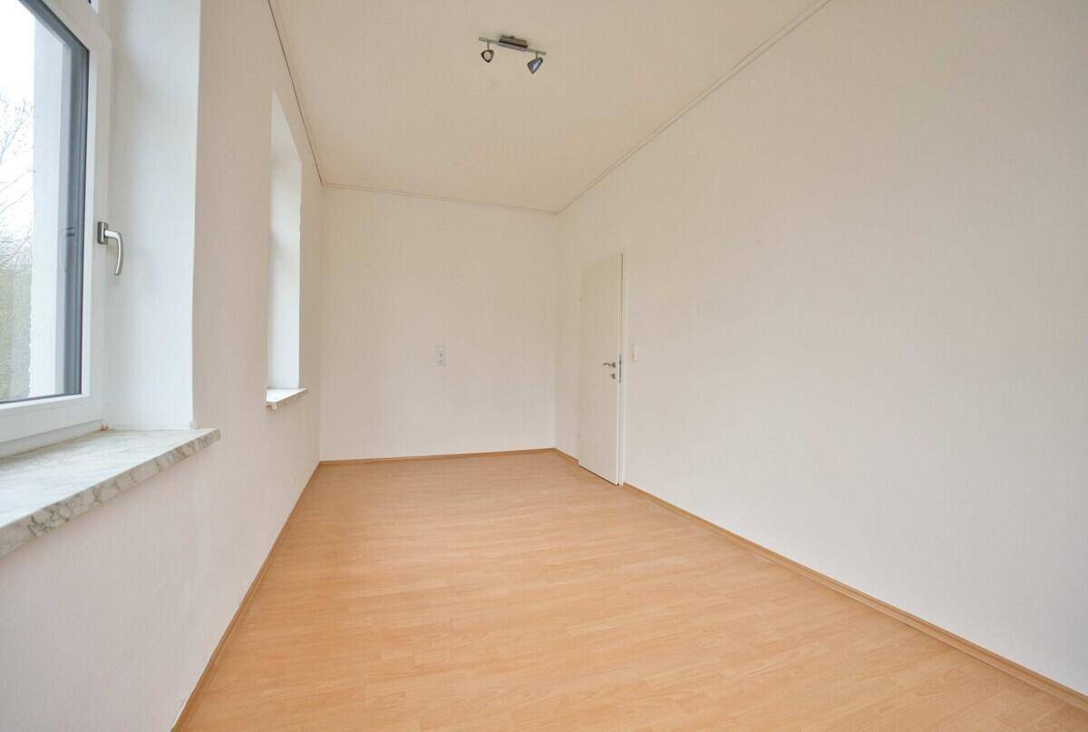 Helles, leeres Zimmer mit Laminatboden und zwei Fenstern, geeignet als Schlaf- oder Arbeitszimmer.