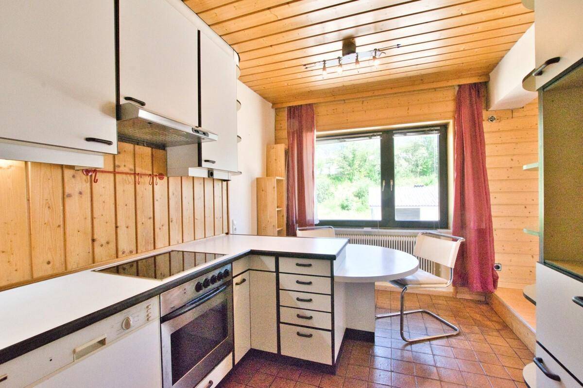 Funktionale Küche mit weißen Einbauschränken, Kochfeld, Backofen und Essbereich am Fenster.