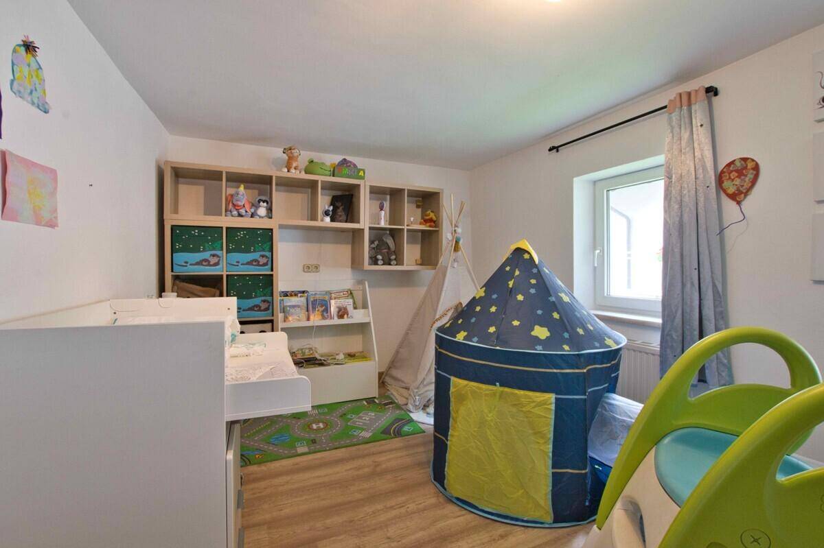 Kinderzimmer mit Spielzelt, Regalen und hellem Fenster.