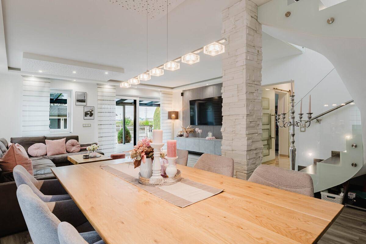 Eleganter Essbereich mit großem Holztisch, moderner Beleuchtung und Blick ins Wohnzimmer.