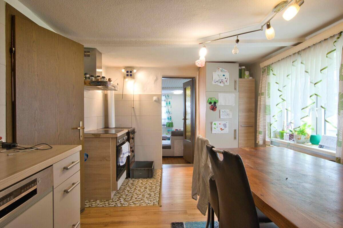 Helle Küche mit Fenster, Kühlschrank und Blick in den angrenzenden Raum.