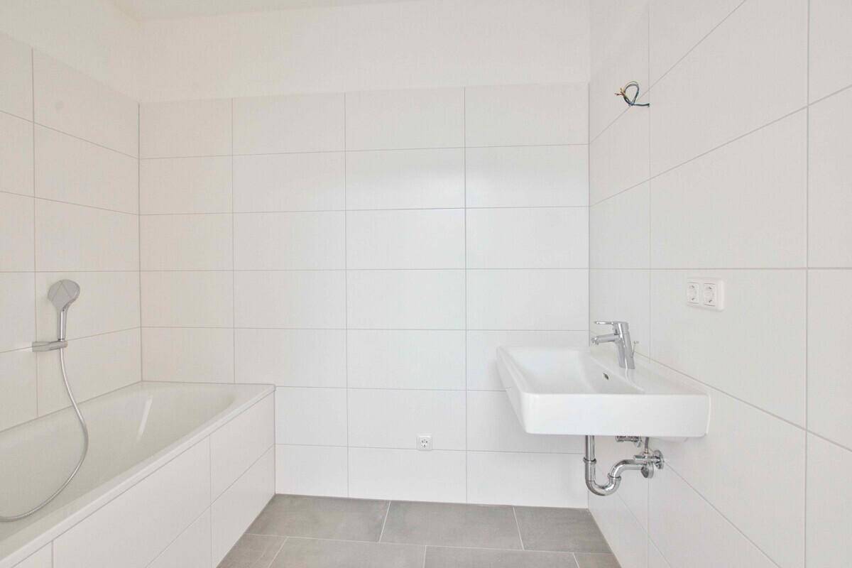 Modernes Badezimmer mit weißen Fliesen, Badewanne und einem einzelnen Waschbecken.