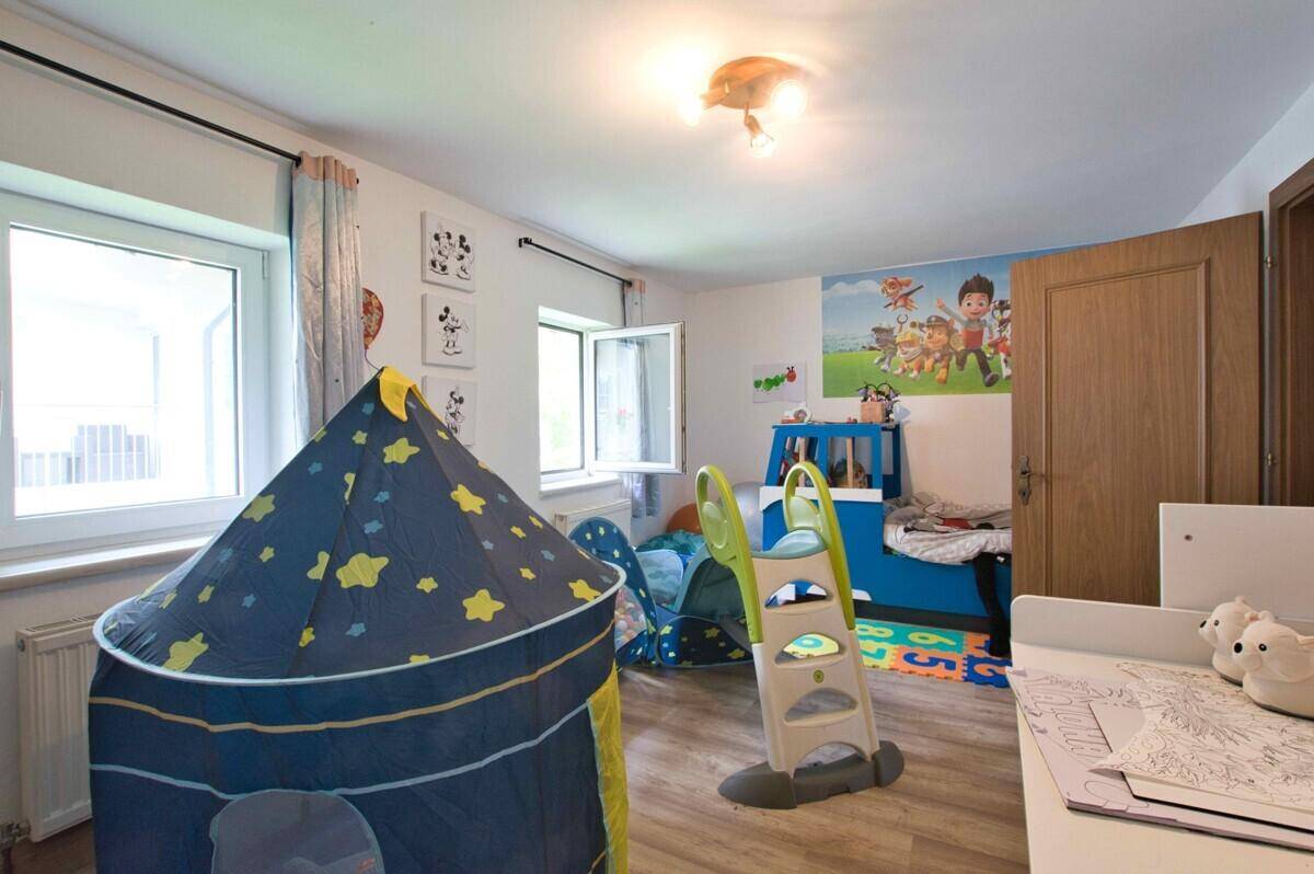 Helles Kinderzimmer mit Spielbereich, Fenster und farbenfrohen Wanddekorationen.