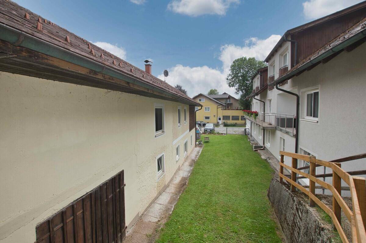 Grünfläche zwischen zwei Gebäuden mit Blick in die Ferne und bewölktem Himmel.