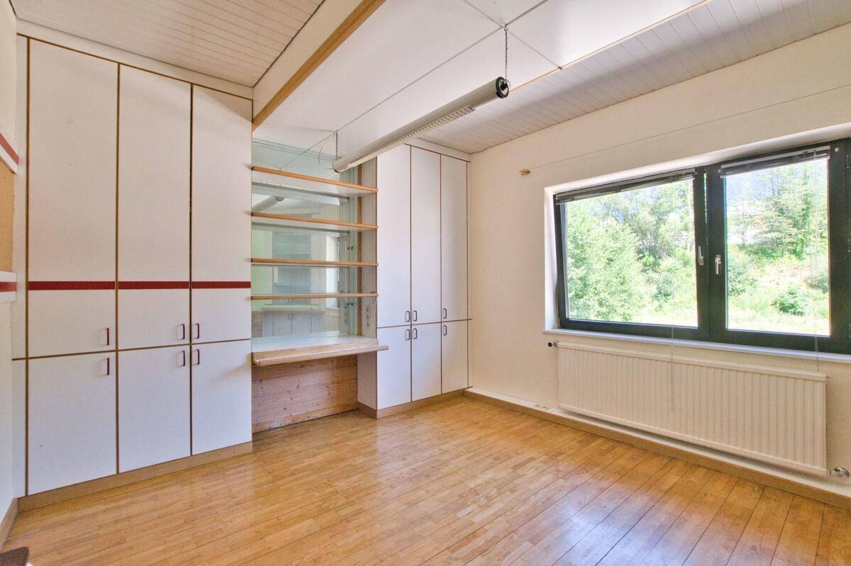 Helles Arbeitszimmer mit Einbauschränken, Holzfußboden und großem Fenster mit Blick ins Grüne.