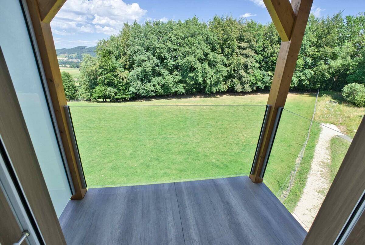Blick von einem kleinen Balkon mit Holzstruktur auf grüne Wiesen und Wald.