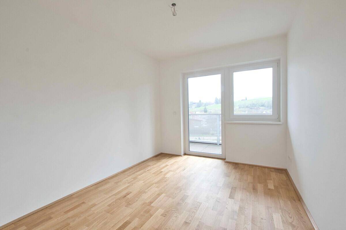 Helles Schlafzimmer mit Holzparkettboden und großen Fenstern.